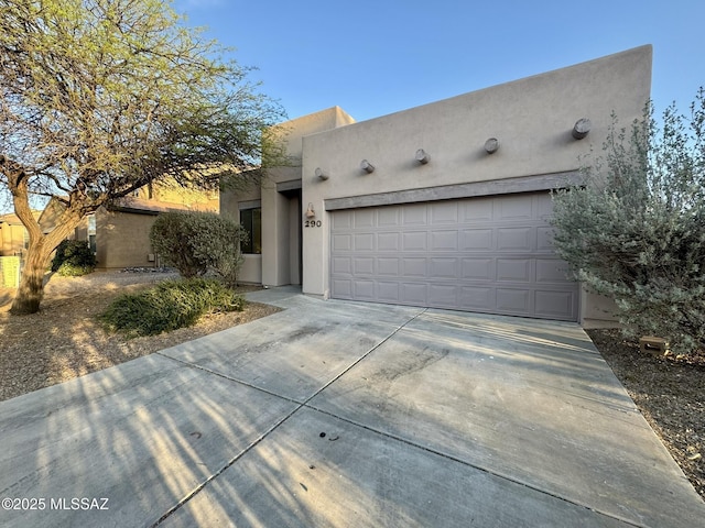 pueblo-style home featuring concrete driveway, an attached garage, and stucco siding