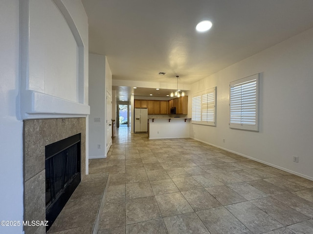unfurnished living room with baseboards, a tile fireplace, and a chandelier