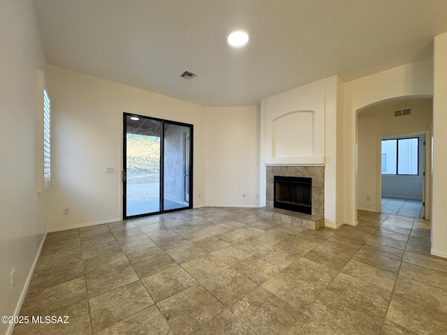 unfurnished living room featuring a fireplace, arched walkways, stone finish floor, baseboards, and visible vents