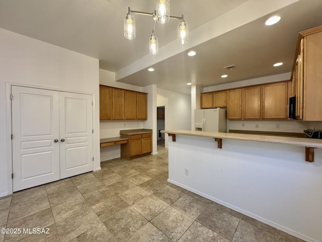 kitchen featuring brown cabinets, white refrigerator with ice dispenser, built in study area, a peninsula, and visible vents