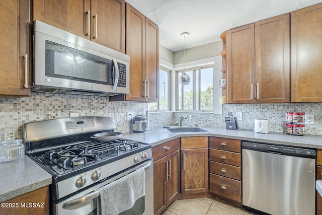 kitchen with brown cabinetry, a sink, backsplash, and stainless steel appliances