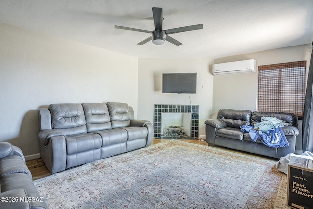 living room featuring a fireplace, an AC wall unit, a ceiling fan, baseboards, and wood finished floors