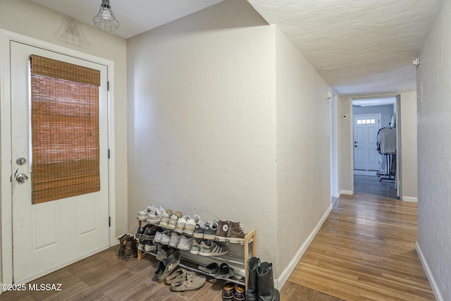 hallway with baseboards, a textured wall, and wood finished floors