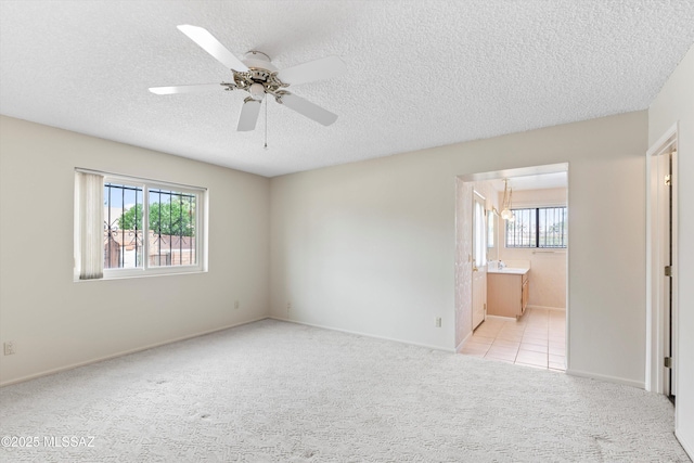 1011 N Placita Yoas, Green Valley, AZ 85614 - unfurnished bedroom featuring a textured ceiling, multiple windows, light carpet, connected bathroom, and baseboards