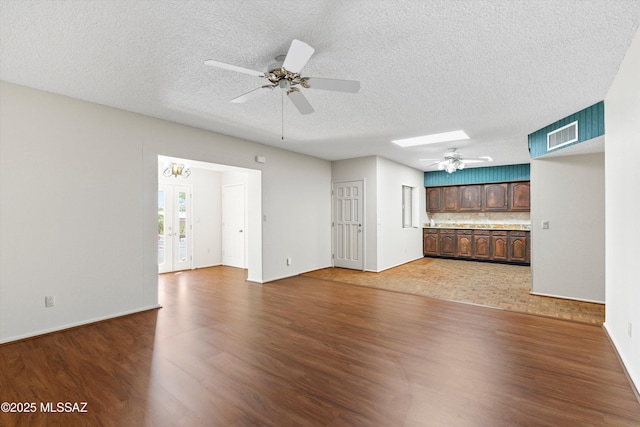 1011 N Placita Yoas, Green Valley, AZ 85614 - unfurnished living room featuring dark wood-style flooring, ceiling fan, a skylight, a textured ceiling, and baseboards