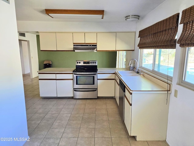 kitchen with light countertops, under cabinet range hood, cream cabinetry, a sink, and stainless steel appliances