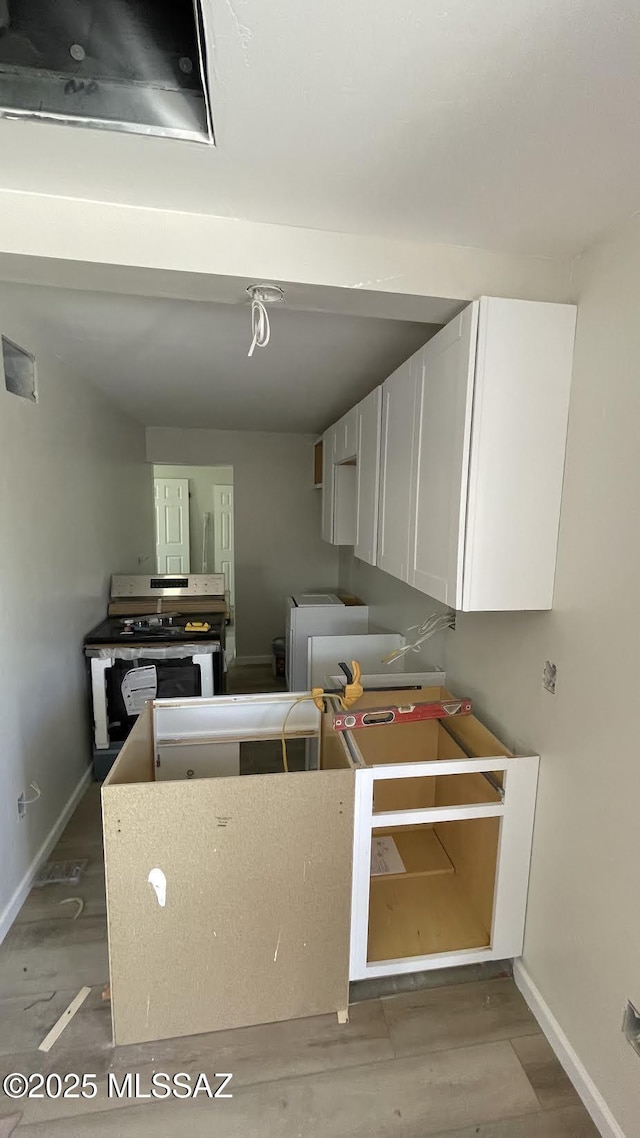 kitchen with white cabinets, baseboards, wood finished floors, and stainless steel range with electric stovetop