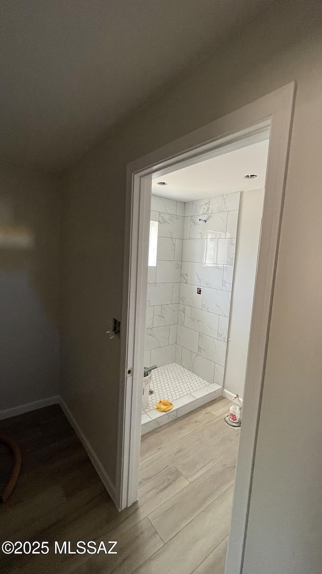 bathroom with baseboards, wood finished floors, and a shower stall