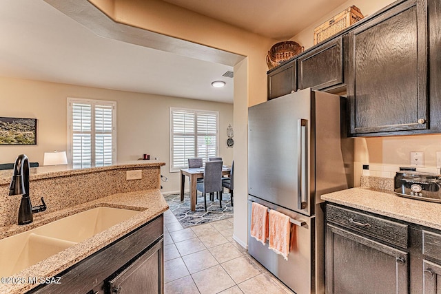 kitchen featuring visible vents, freestanding refrigerator, dark brown cabinetry, a sink, and light tile patterned floors