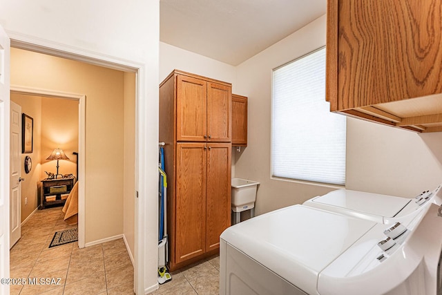 laundry area featuring baseboards, washing machine and clothes dryer, a sink, cabinet space, and light tile patterned floors