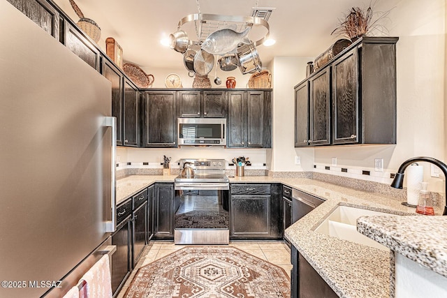 kitchen featuring light tile patterned flooring, appliances with stainless steel finishes, light stone counters, a sink, and visible vents
