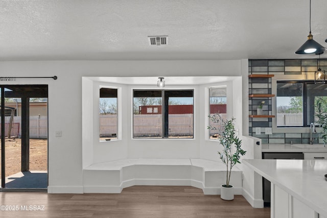 unfurnished dining area with visible vents, wood finished floors, baseboards, a textured ceiling, and a sink