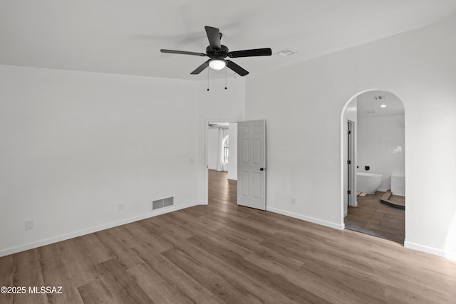 unfurnished bedroom with arched walkways, baseboards, visible vents, and wood finished floors