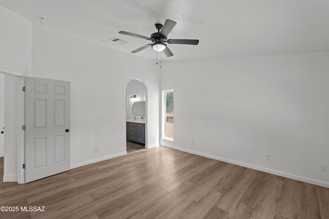 spare room featuring a ceiling fan, visible vents, arched walkways, wood finished floors, and baseboards