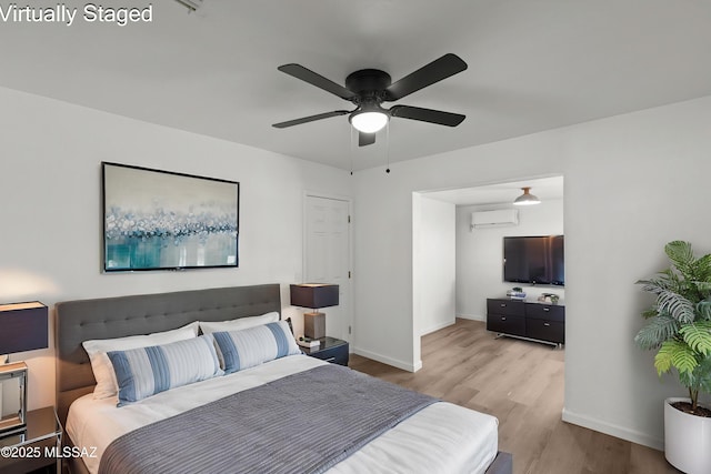 bedroom with wood finished floors, baseboards, ceiling fan, and a wall unit AC