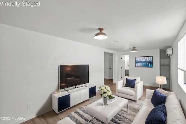 living area with an AC wall unit, visible vents, plenty of natural light, and light wood-style floors