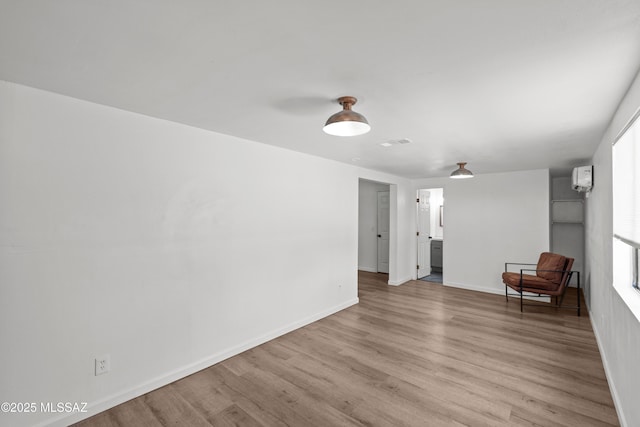 interior space with light wood-style floors, a wall mounted air conditioner, and baseboards