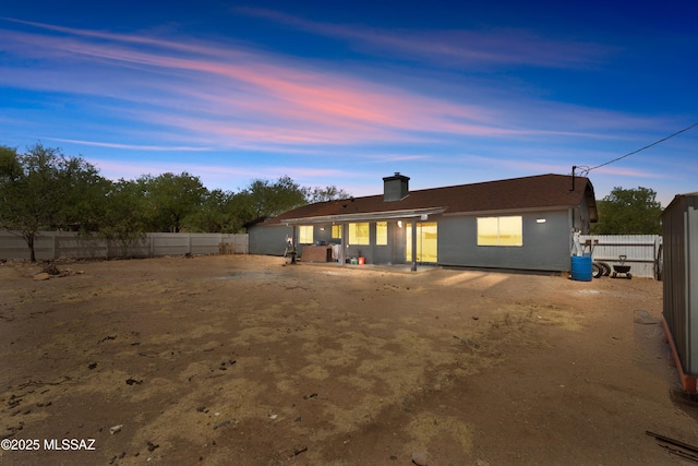 back of house at dusk with a fenced backyard and a chimney