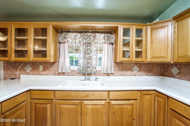 kitchen featuring a sink, glass insert cabinets, tasteful backsplash, and light countertops