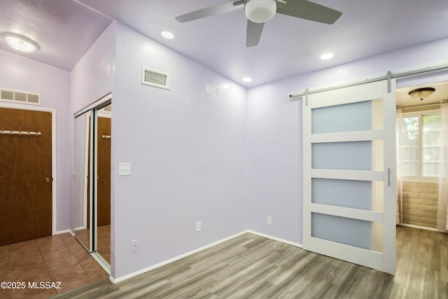 unfurnished bedroom with wood finished floors, a barn door, and visible vents