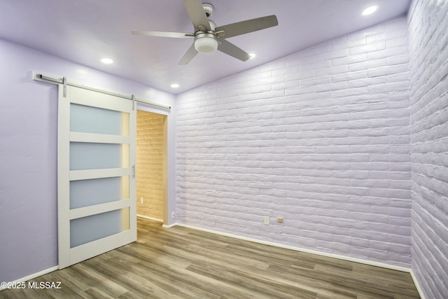unfurnished bedroom featuring ceiling fan, a barn door, recessed lighting, baseboards, and wood finished floors