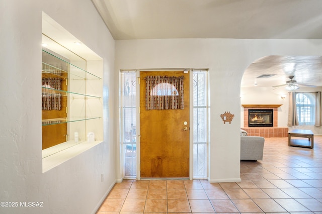 tiled entrance foyer with ceiling fan, visible vents, a tiled fireplace, arched walkways, and baseboards