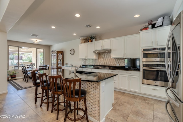 kitchen with gas cooktop, under cabinet range hood, white cabinets, a sink, and backsplash
