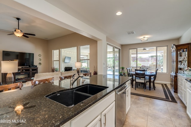 kitchen with white cabinets, a sink, dark stone countertops, open floor plan, and stainless steel dishwasher