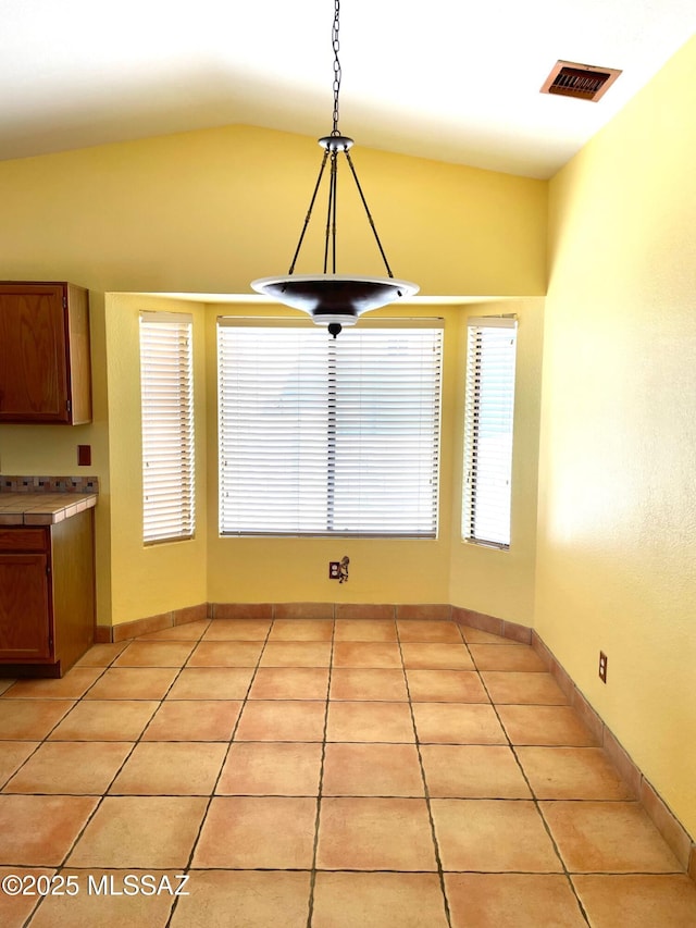 unfurnished dining area featuring light tile patterned flooring, visible vents, and lofted ceiling