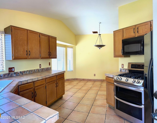 kitchen featuring black microwave, tile counters, refrigerator with ice dispenser, vaulted ceiling, and double oven range