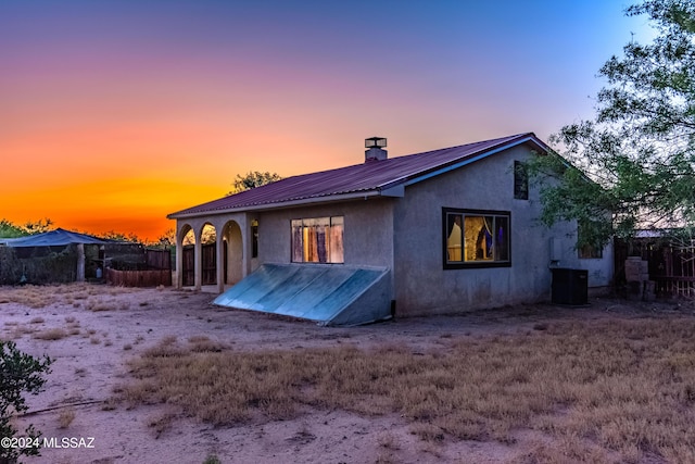 back of property at dusk featuring cooling unit, stucco siding, and metal roof