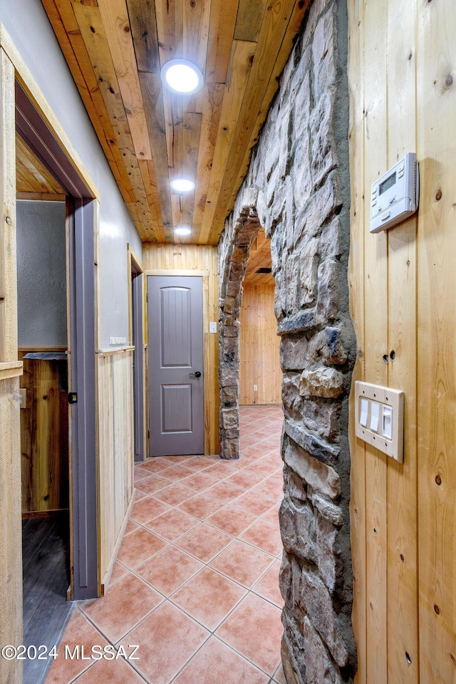 hallway with wood ceiling, arched walkways, wainscoting, tile patterned floors, and wooden walls