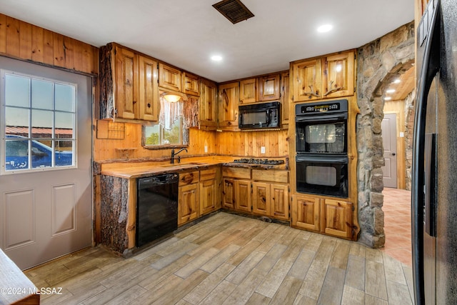 kitchen with brown cabinets, a sink, light wood-style floors, light countertops, and black appliances