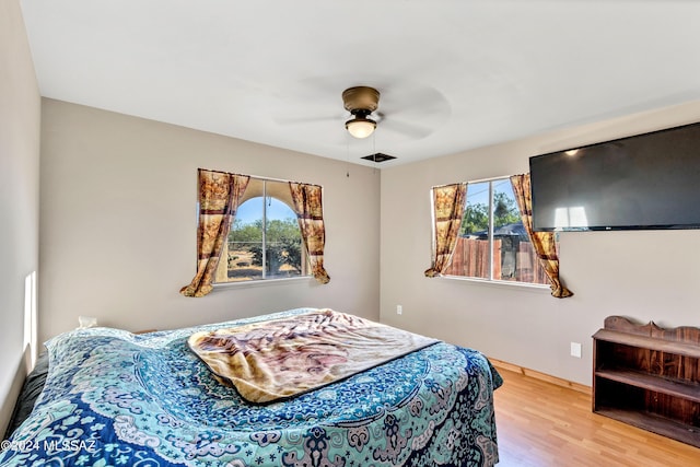 bedroom featuring baseboards, ceiling fan, multiple windows, and wood finished floors