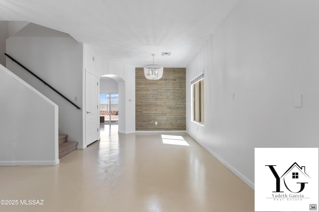 unfurnished living room featuring arched walkways, baseboards, finished concrete floors, visible vents, and stairway