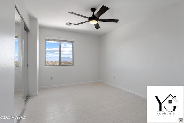 spare room featuring visible vents, a ceiling fan, light wood-style floors, and baseboards