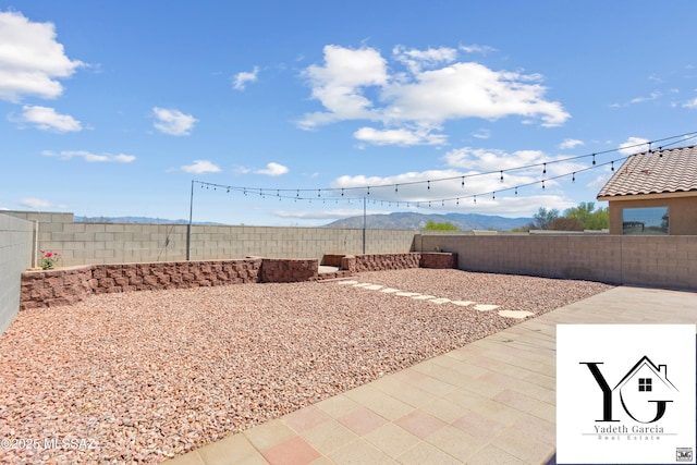 view of yard featuring a patio, a mountain view, and a fenced backyard