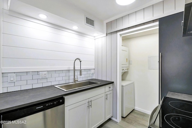 kitchen with stacked washer / dryer, visible vents, dark countertops, stainless steel dishwasher, and a sink