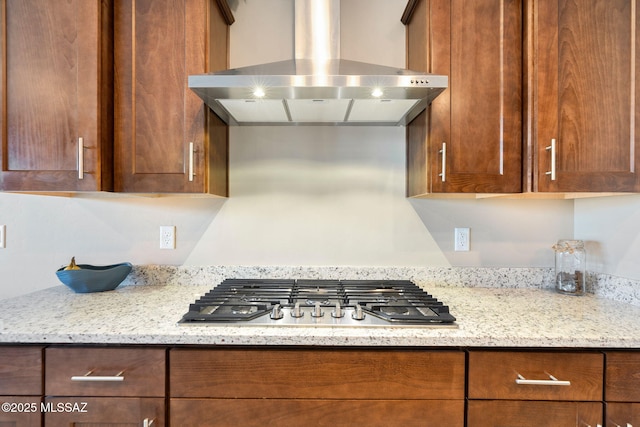 7084 W Cliff Spring Trl, Marana, AZ 85658 - kitchen featuring wall chimney exhaust hood, stainless steel gas cooktop, light stone countertops, and brown cabinets