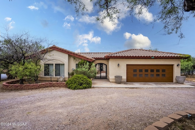 mediterranean / spanish-style home with a garage, stucco siding, driveway, and a tiled roof