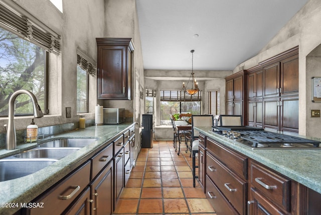 kitchen featuring hanging light fixtures, light tile patterned floors, a sink, a notable chandelier, and stainless steel gas stovetop