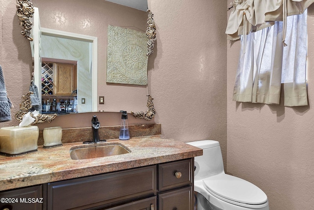 half bathroom with vanity, a textured wall, and toilet