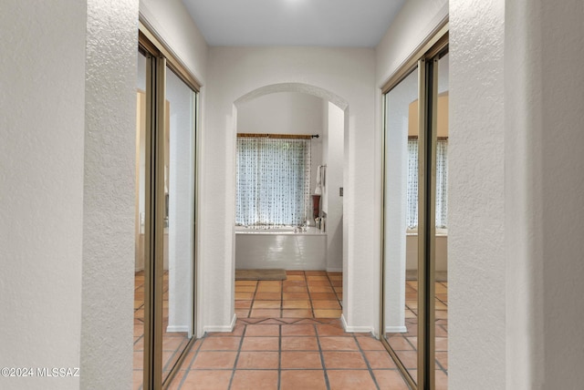 corridor with tile patterned flooring, arched walkways, and a textured wall