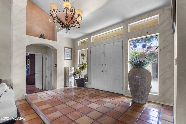 tiled entryway featuring arched walkways, a high ceiling, and a notable chandelier
