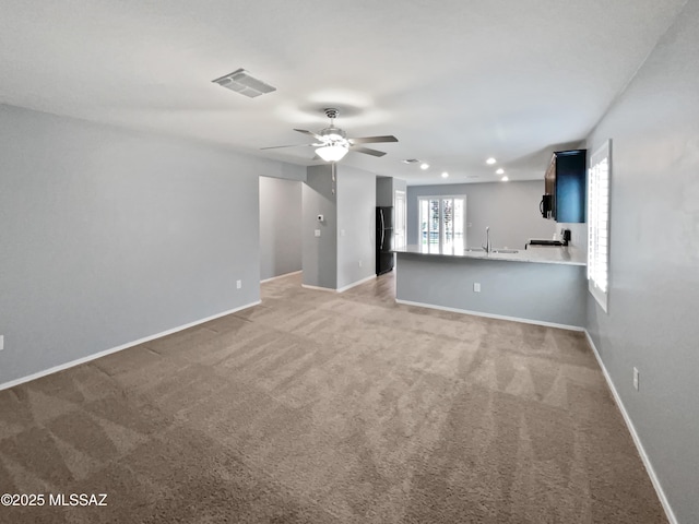 unfurnished living room with a sink, a ceiling fan, light colored carpet, and visible vents