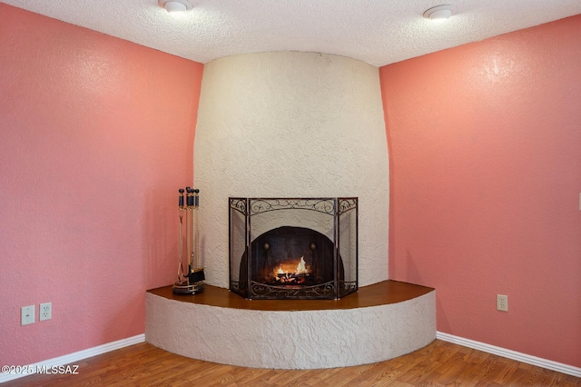 details with a textured ceiling, a textured wall, wood finished floors, and a large fireplace