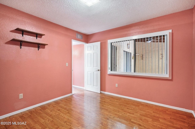 spare room with a textured ceiling, baseboards, wood finished floors, and visible vents