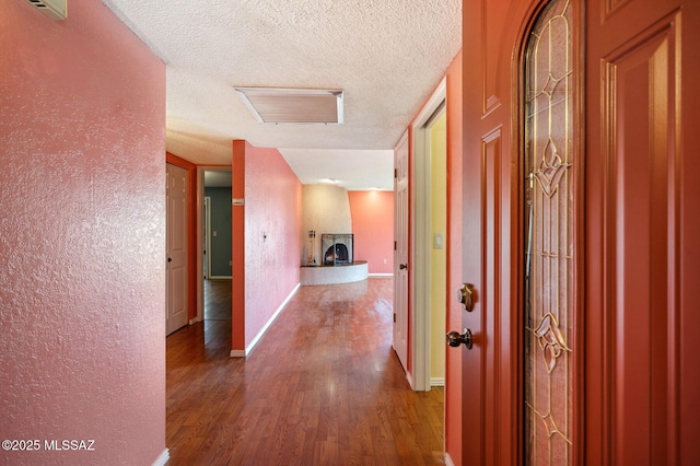 corridor with dark wood-style flooring, a textured ceiling, a textured wall, and baseboards