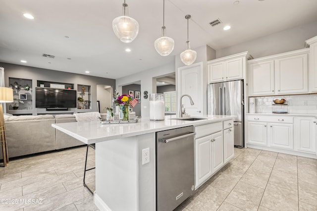 kitchen with an island with sink, white cabinets, tasteful backsplash, a sink, and stainless steel appliances