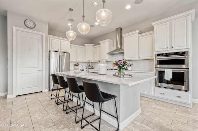 kitchen with wall chimney range hood, appliances with stainless steel finishes, tasteful backsplash, and light countertops